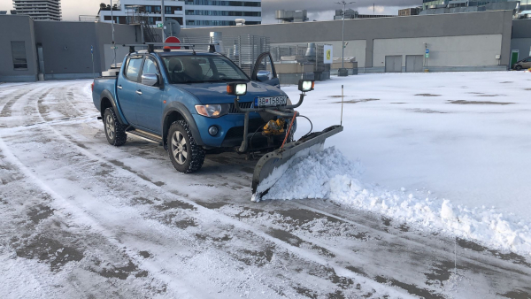 Modré vozidlo Mitsubishi L200 spoločnosti STONE TRADE s prednou radlicou pri čistení snehu na strešnom parkovisku.