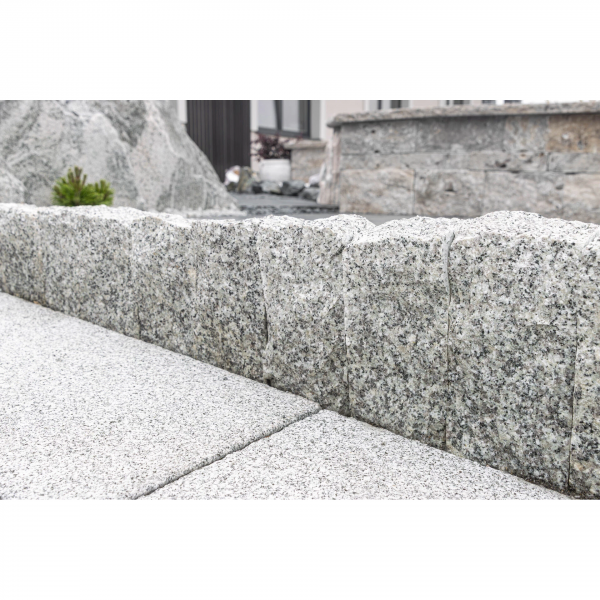 Detailné zobrazenie štiepaného povrchu žulovej palisády Bianco Nero od STONE TRADE použitej ako nízky okrasný obrubník pri svetlej dlažbe.