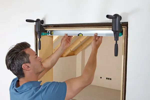 Pracovník používa montážne rozpery Wolfcraft Pro a vodováhu na presné vyrovnanie a upevnenie dvernej zárubne v interiéri od stonetrade.  Prehľad série Wolfcraft Pro: