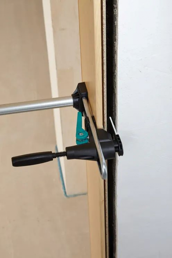 Detailný záber na bočné upevnenie montážnej rozpery Wolfcraft Pro, ktorá fixuje dvernú zárubňu k stene počas schnutia montážnej peny od stonetrade.